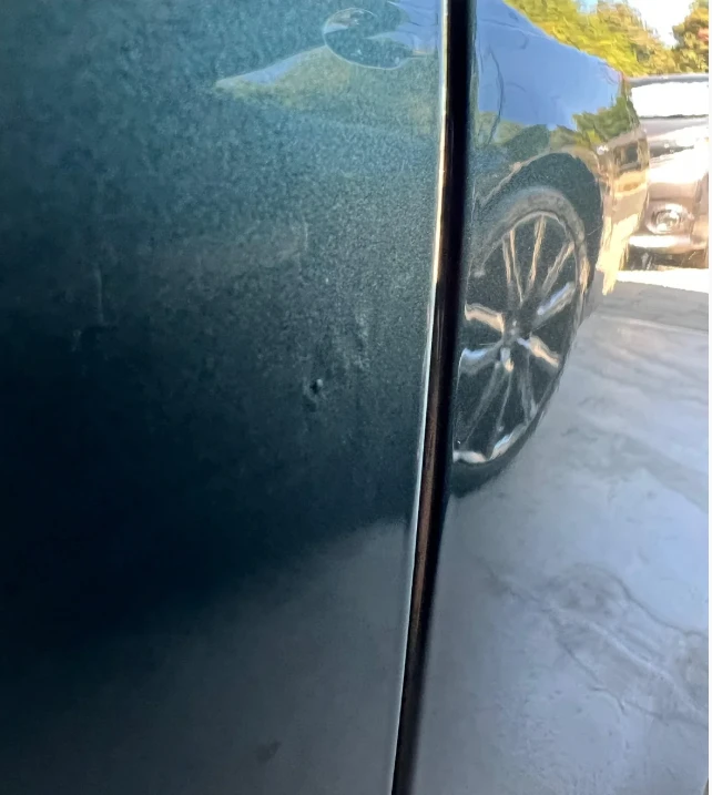 Dark teal car panel covered in bumps and heavy distortion from a botched paintless dent repair