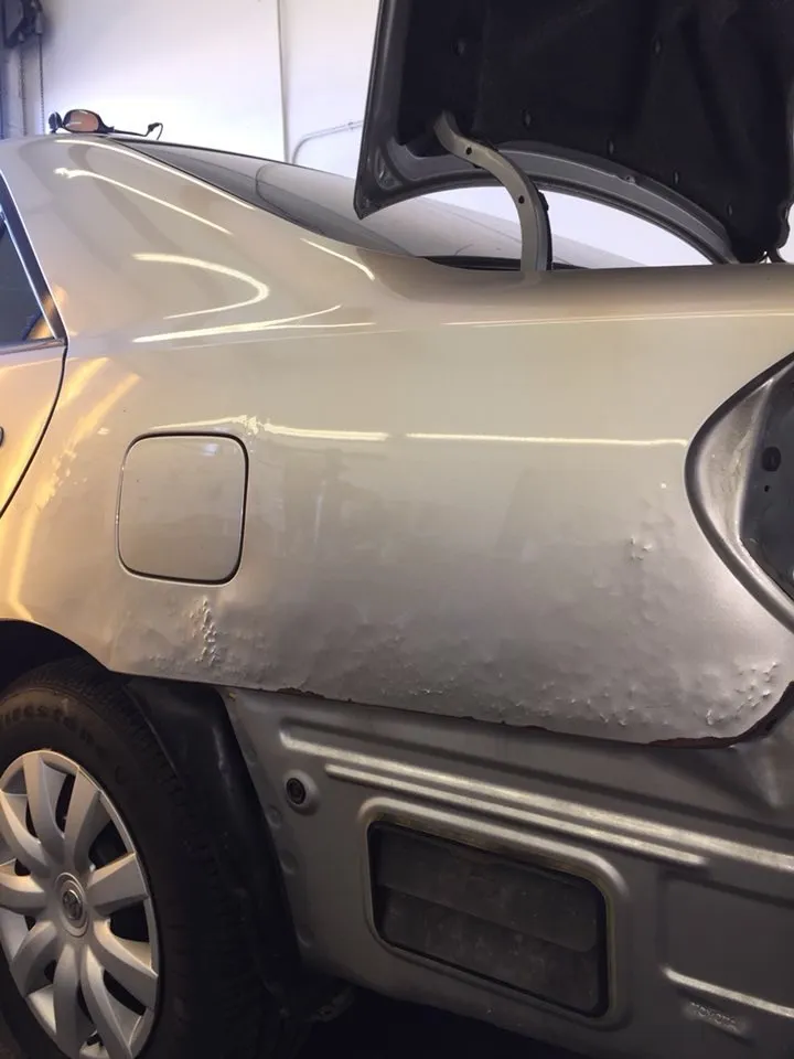 Toyota rear quarter panel in primer with a bubbled, pitted surface from rust and filler under the paint