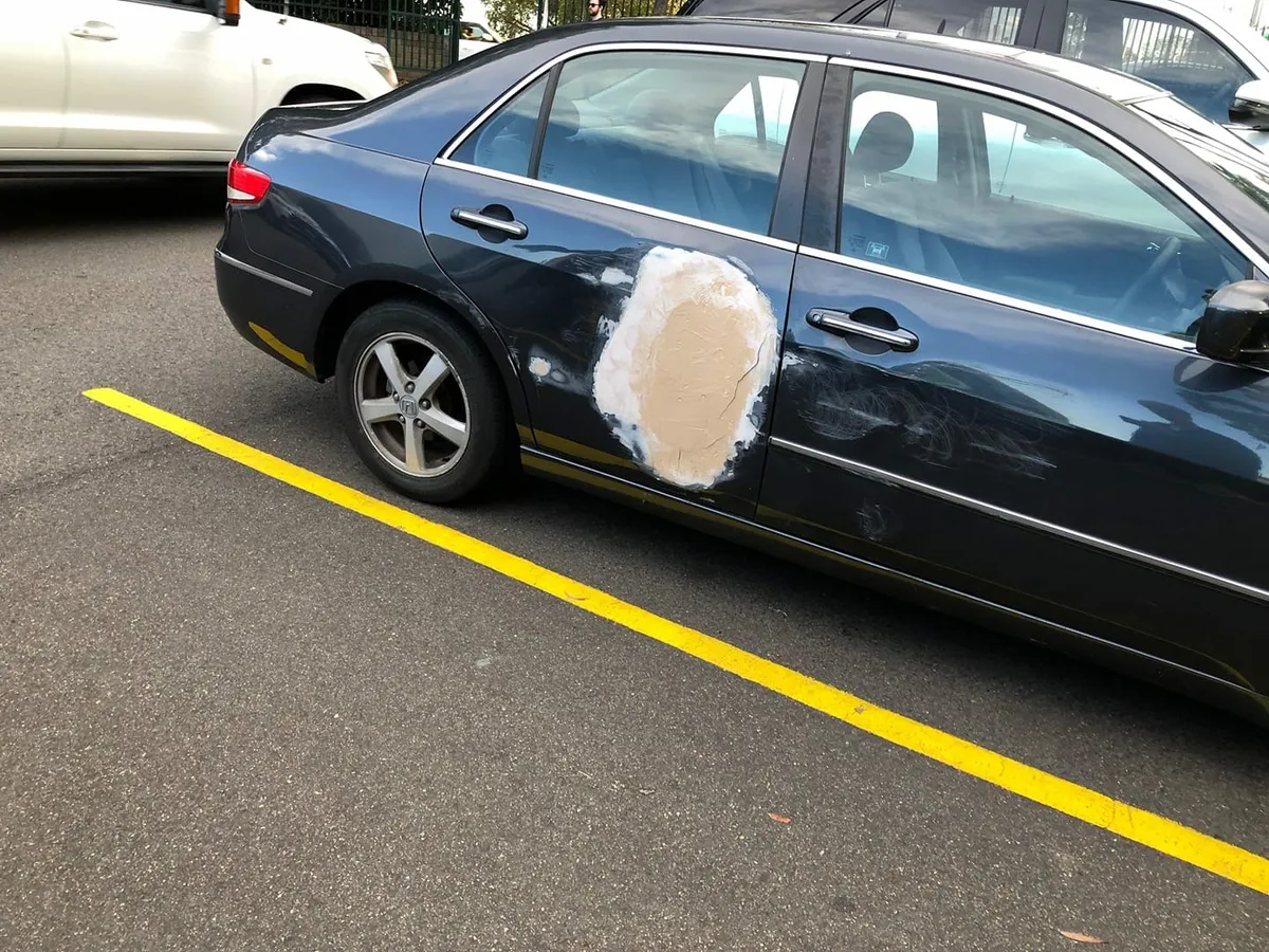 Dark Honda sedan with a raw, unpainted body filler patch on the rear door