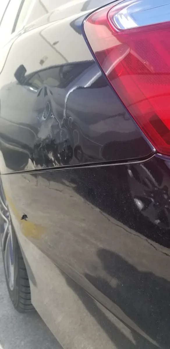 Cracked, blistered paint on a black car near the taillight from an over-pushed dent repair