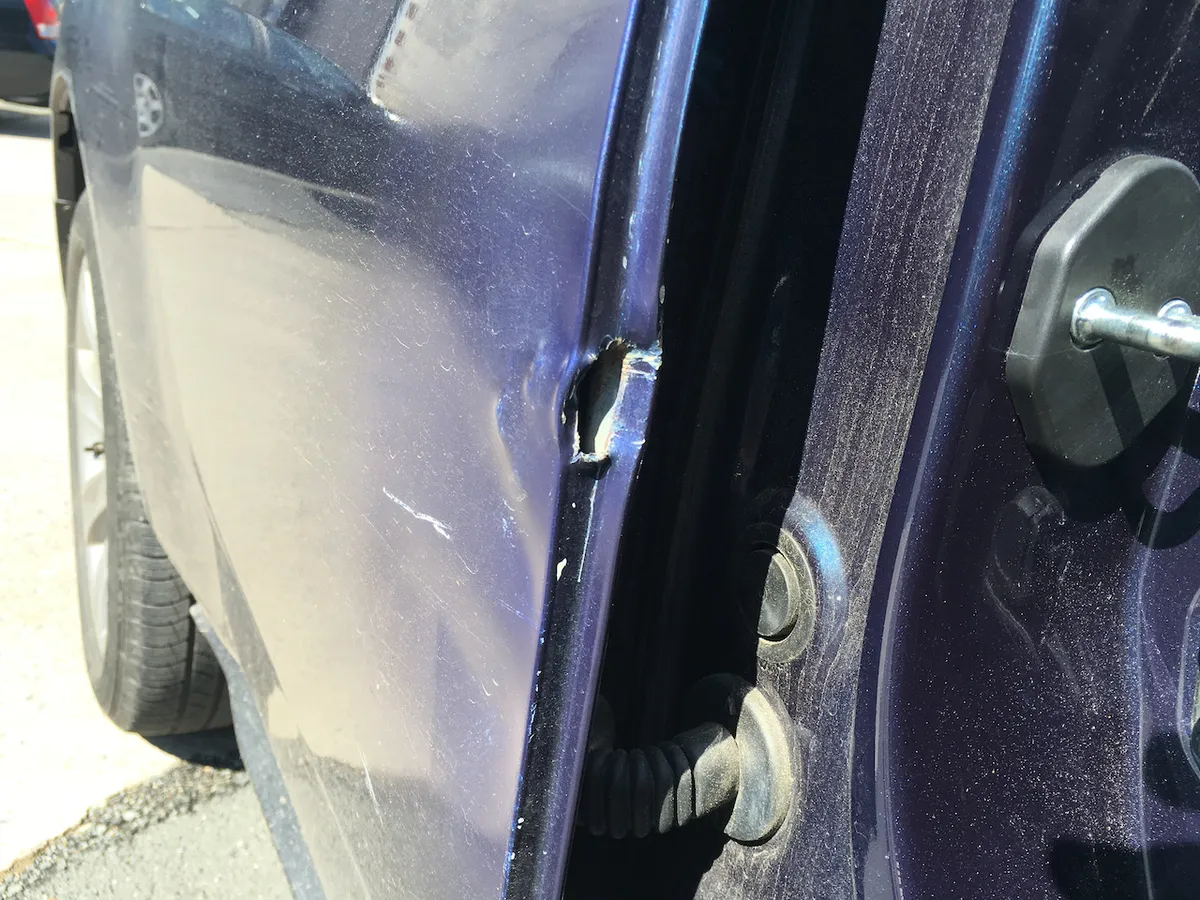 Cracked, lifting paint at a car door edge from a repair forced over a body line