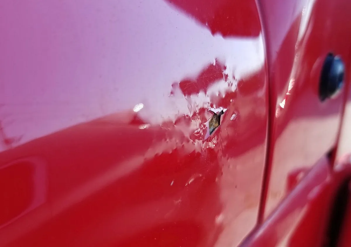 Red car door with metal torn open and clearcoat cracked around it from an over-pushed dent