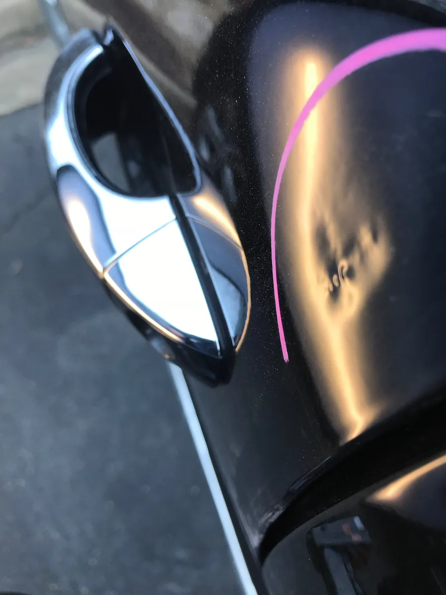 A black panel under a reflector board showing a wavy, dimpled surface from a bad dent repair