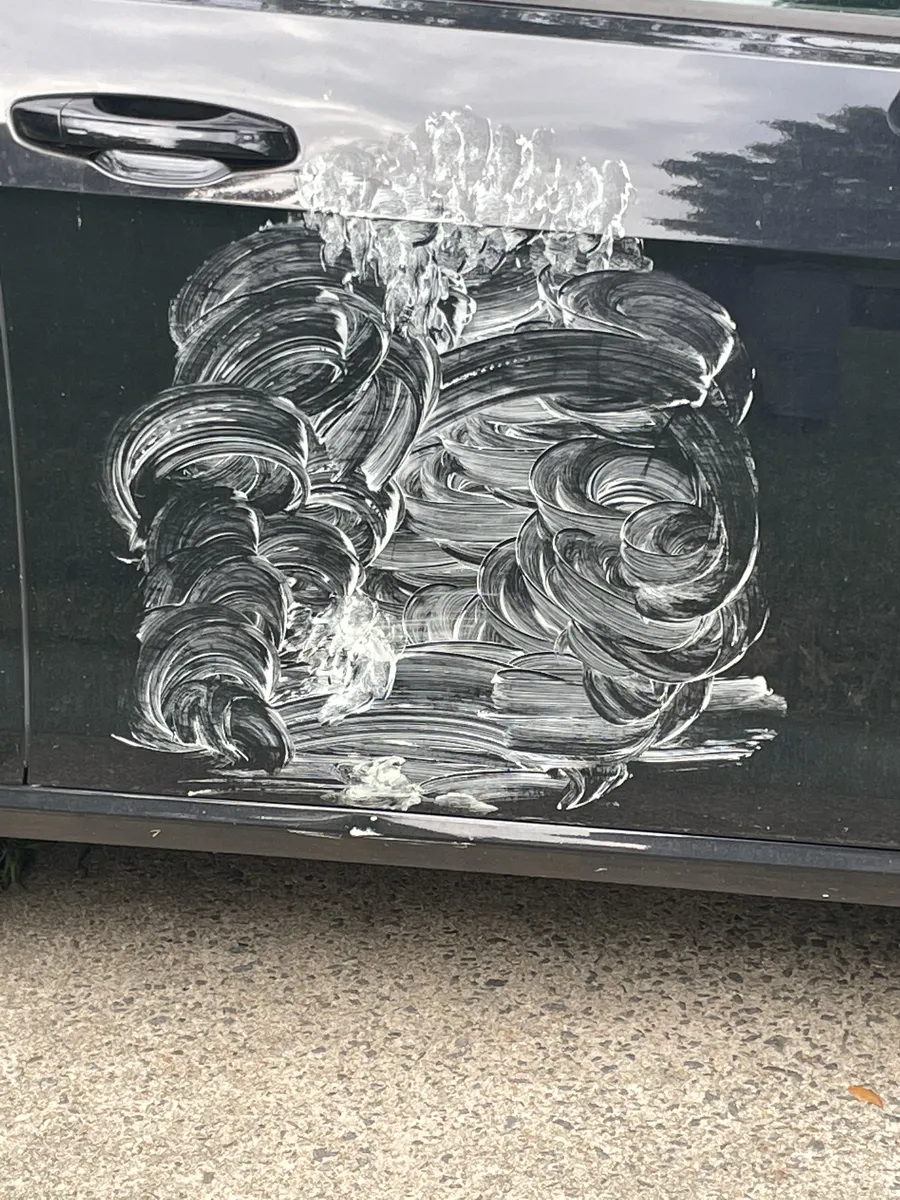 Body filler smeared in swirls over a dent on a black car door