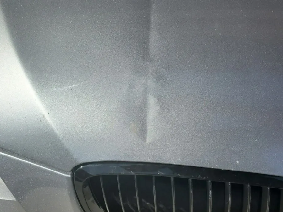 Raised high spot and stressed clearcoat on a silver BMW hood left by a sharp tool